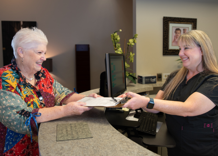 Smiling dental assistant at Dr. Simmons's Plano dental office happily providing new patient forms.