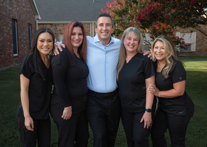 Dr. Thomas Simmons, dentist in Plano, warmly embracing his dedicated dental team in front of our Plano dental office.